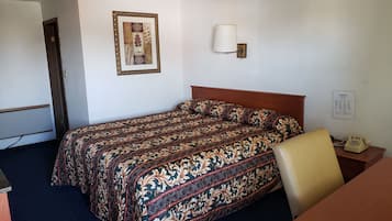A hotel room with a bed, a desk, a chair, a lamp, and a framed picture on the wall.