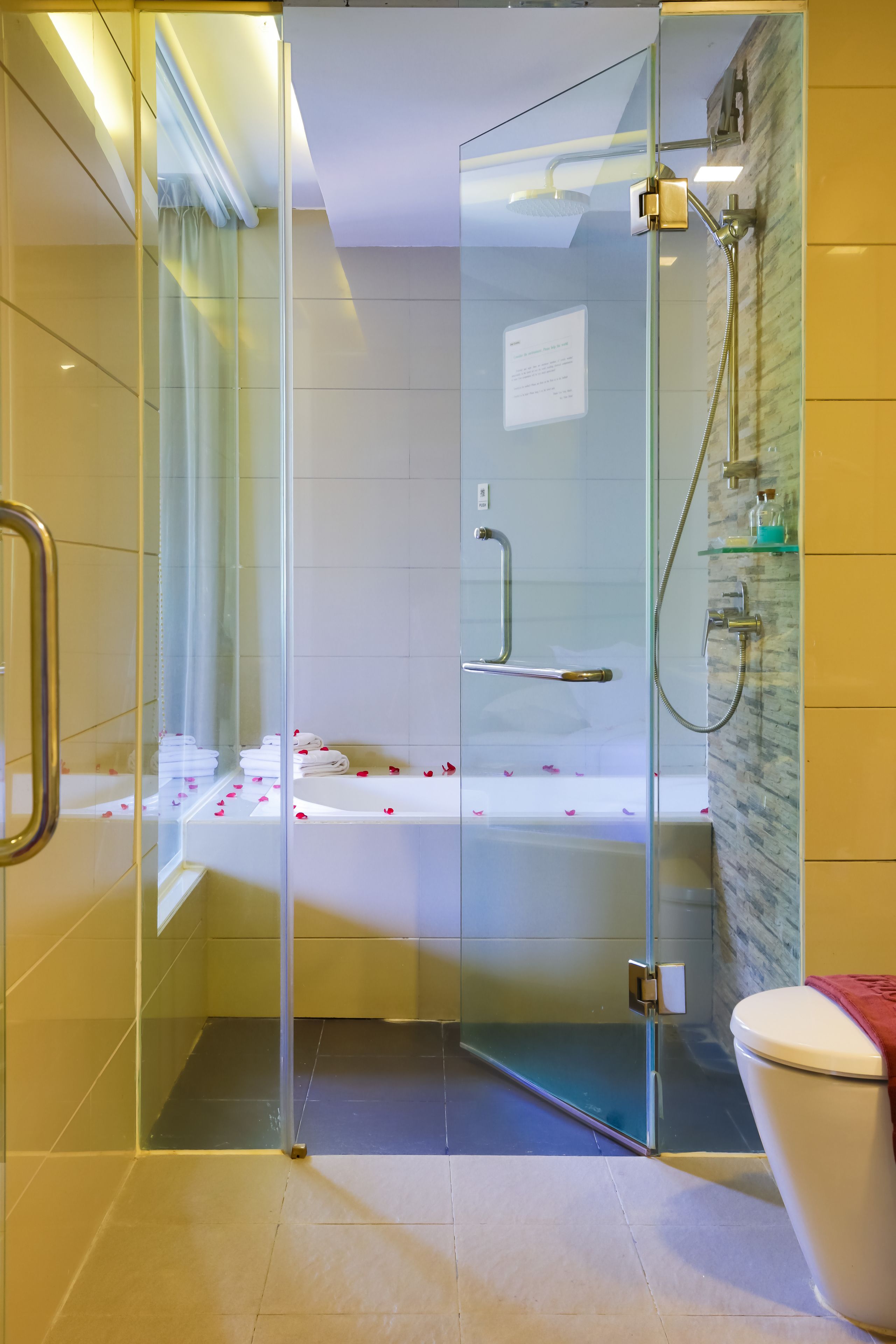 Un baño moderno con ducha de vidrio, una bañera con pétalos de rosa y un inodoro.