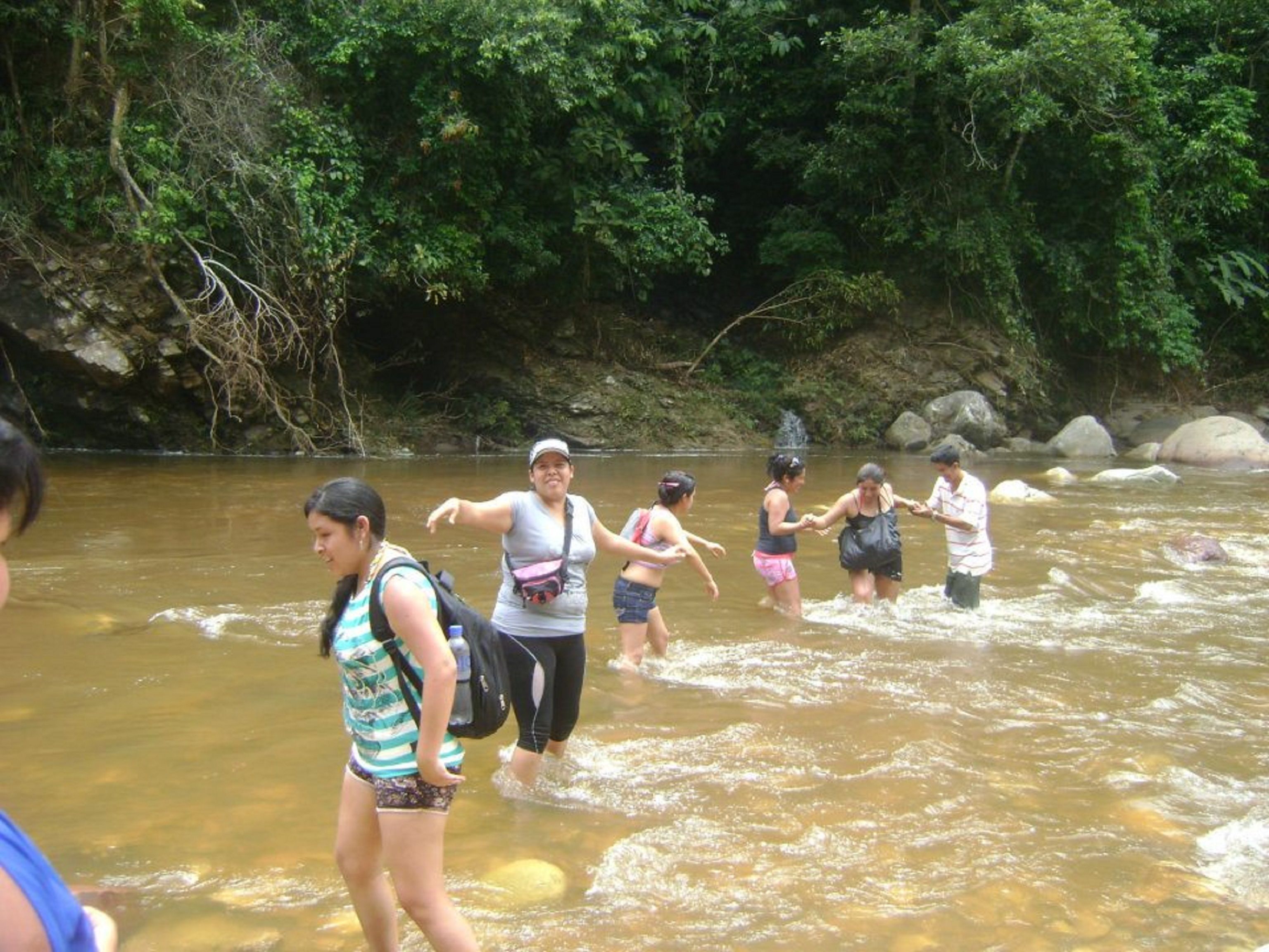 A group of people wading through a river surrounded by dense greenery.