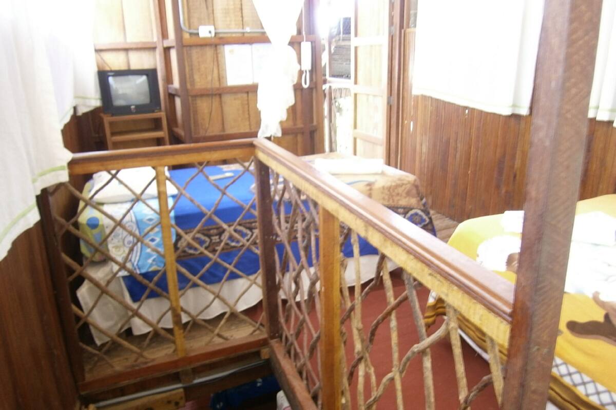 Una habitación con una cama de madera, una mesita, un televisor y una ventana con cortinas.
