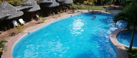 Una piscina rodeada de cabañas con techo de paja y palmeras.