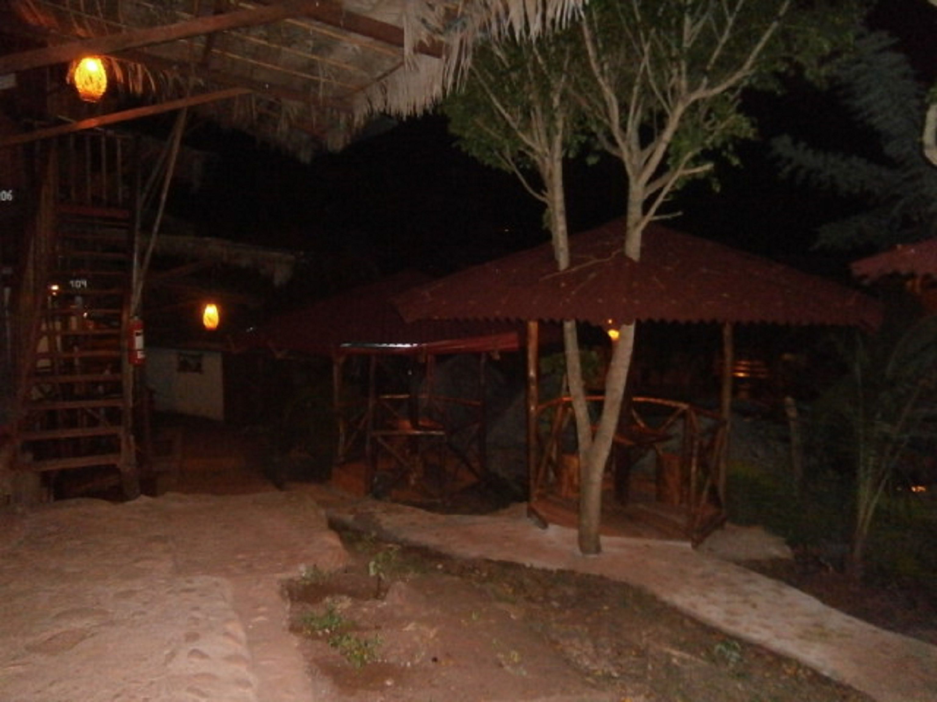 Un espacio exterior rústico con una escalera de madera, una estructura de techo de paja y una zona de estar cubierta.
