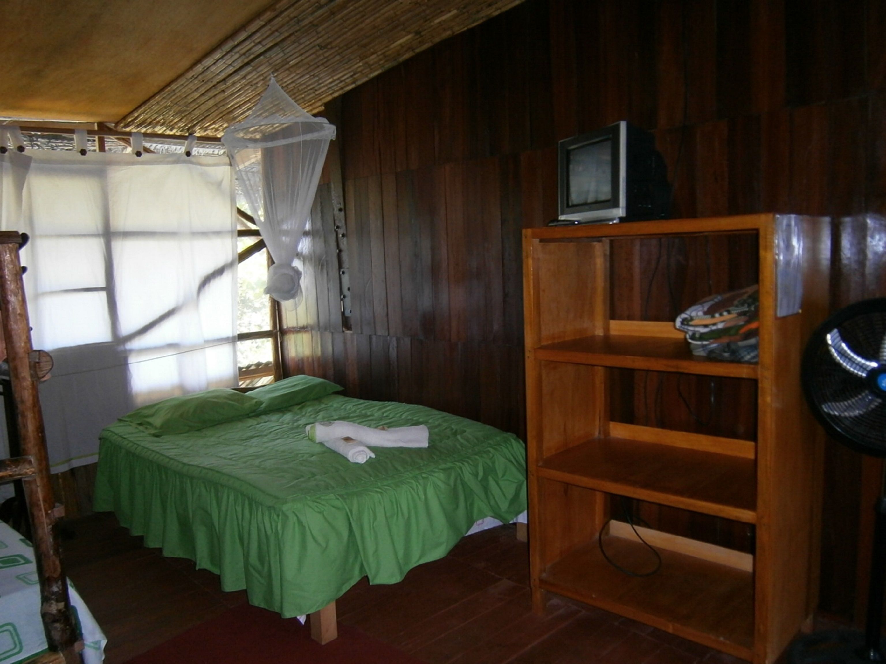 Una habitación con una cama, un estante de madera, un televisor y una mosquitera.
