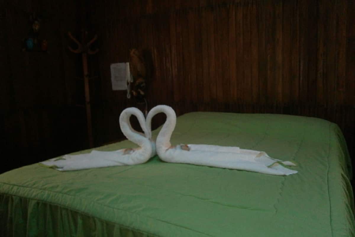 Una cama con un edredón verde y dos toallas dispuestas en forma de cisnes.