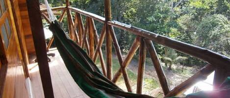 Une terrasse en bois avec un hamac et une balustrade en bois, donnant sur une zone boisée.