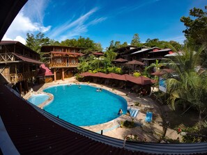 A large outdoor swimming pool surrounded by wooden structures and palm trees. - Madera Labrada Lodge (Tarapoto)