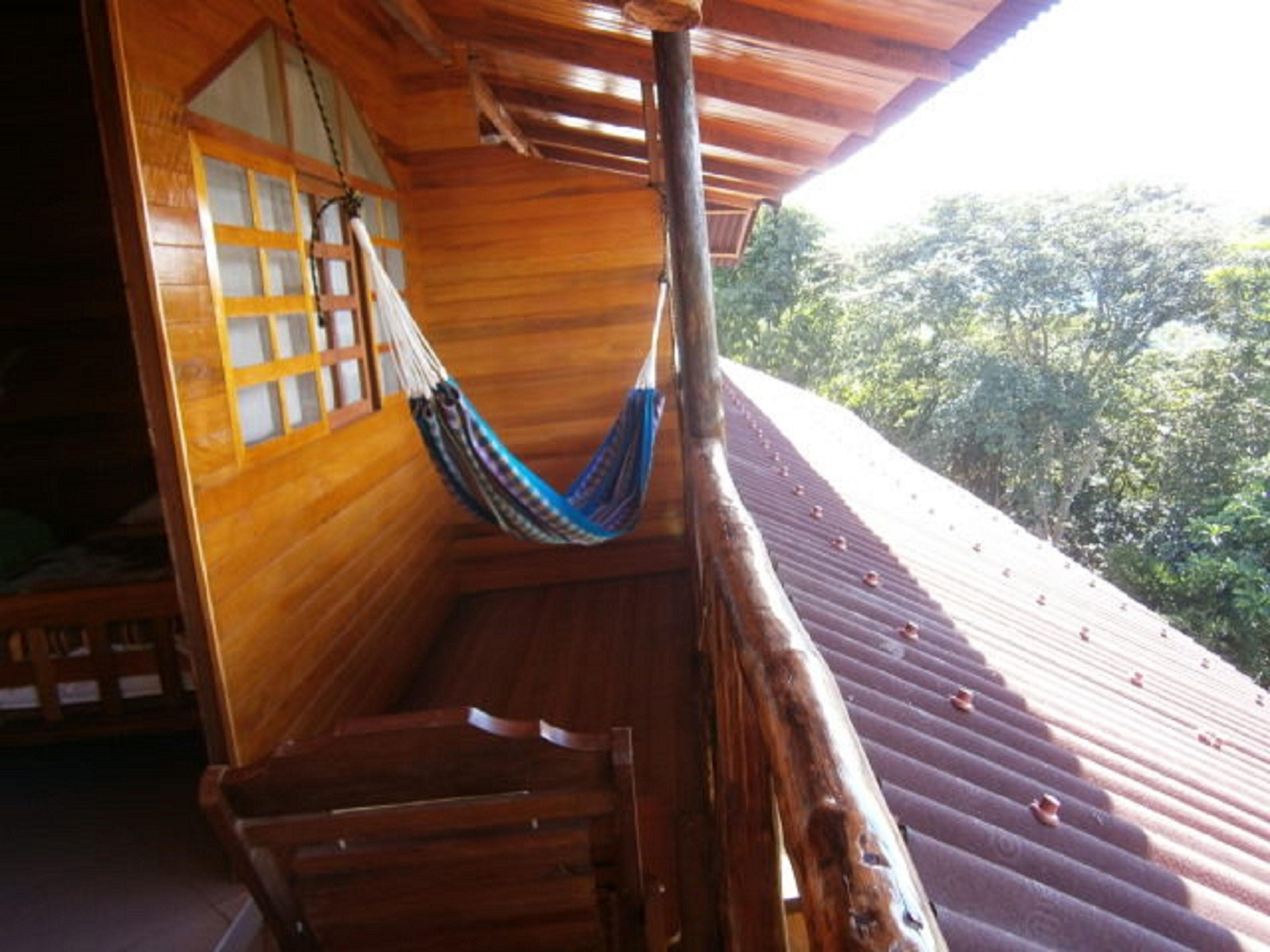 A wooden balcony with a hammock, a wooden staircase, and a view of trees.