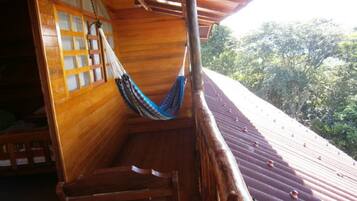 A wooden balcony with a hammock, a wooden staircase, and a view of trees.