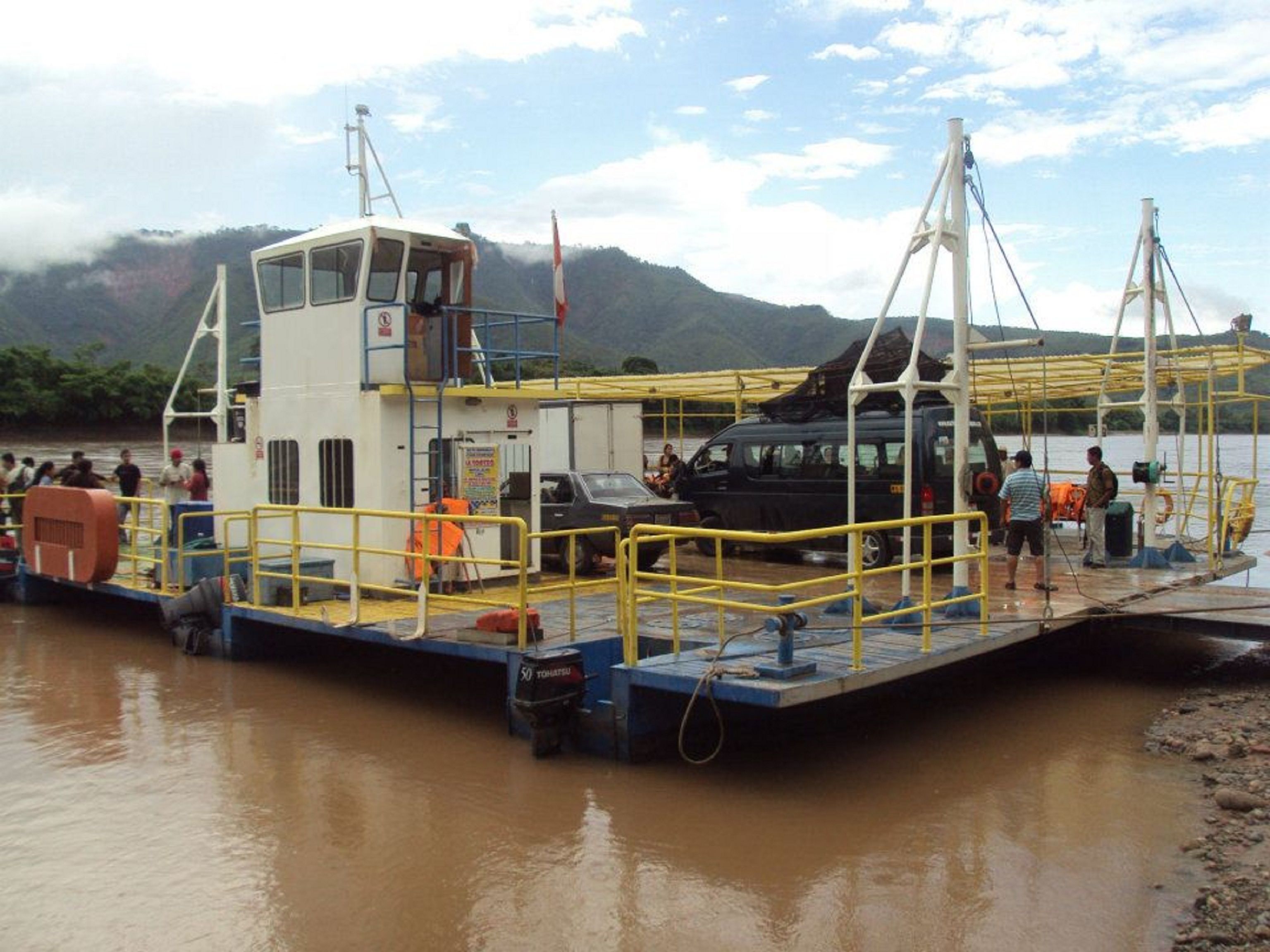 A ferry docked at a river with passengers and vehicles on board.