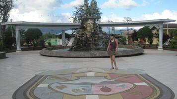 A tiled plaza with a fountain and a statue in the center, surrounded by a covered walkway.