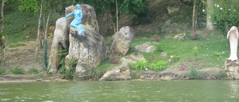 Una estatua de una mujer sentada sobre una roca junto a un río.