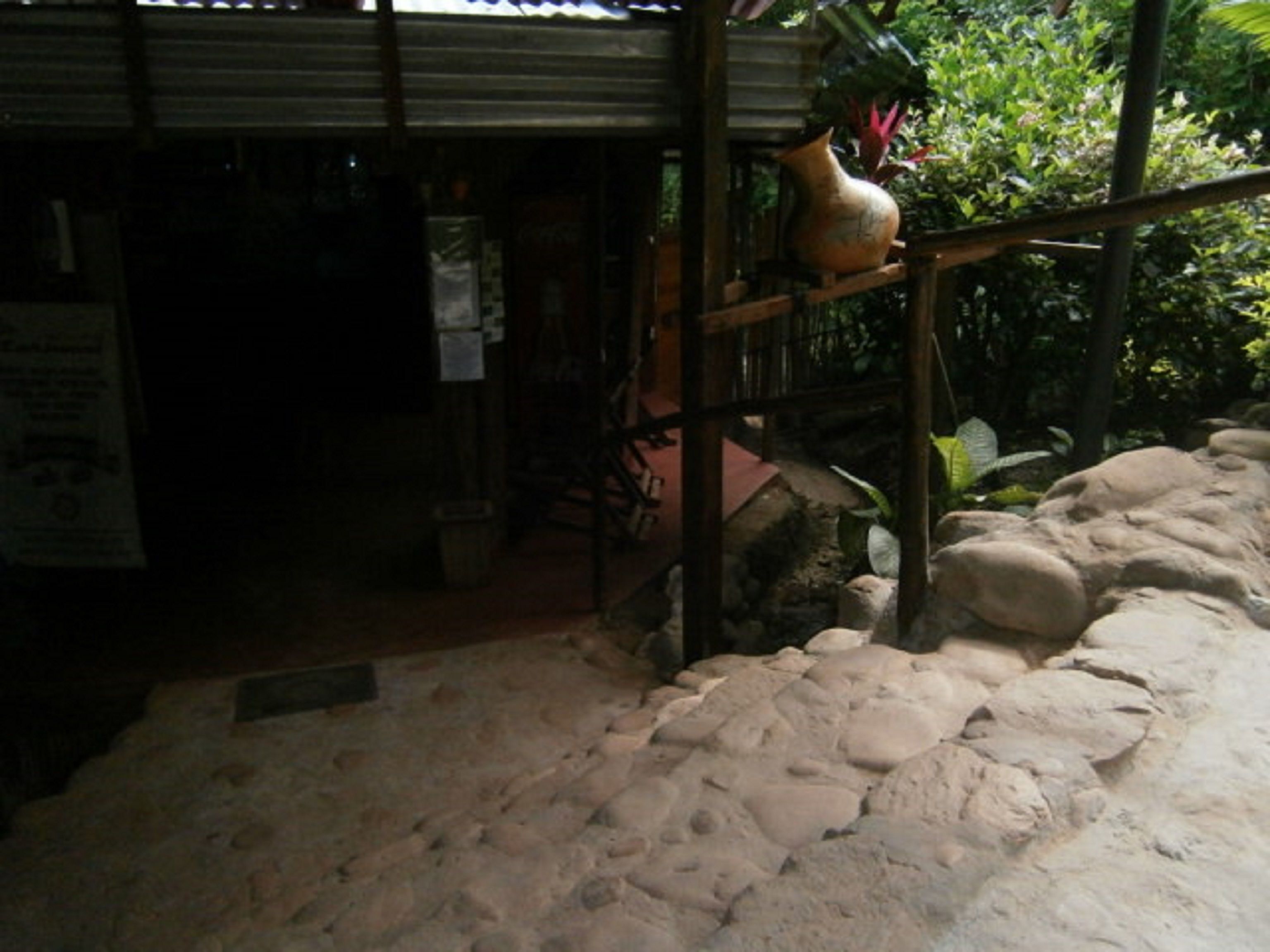 A rustic outdoor area with a stone pathway, a wooden structure, and a large clay pot.