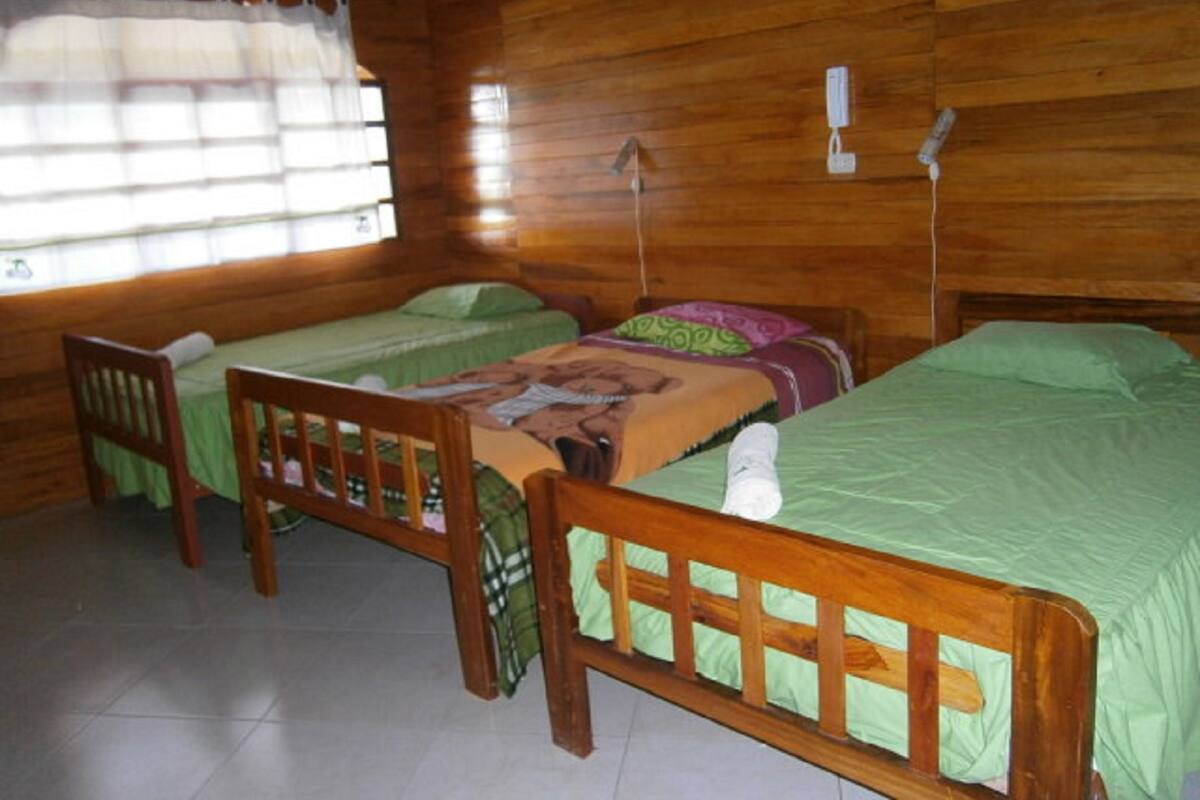 Una habitación con dos camas de madera, una silla y un ventanal con cortinas.