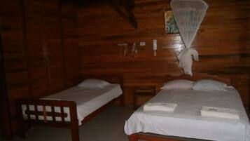 Une chambre dans un chalet en bois, avec deux lits simples, un banc en bois et une moustiquaire au-dessus d’un des lits.