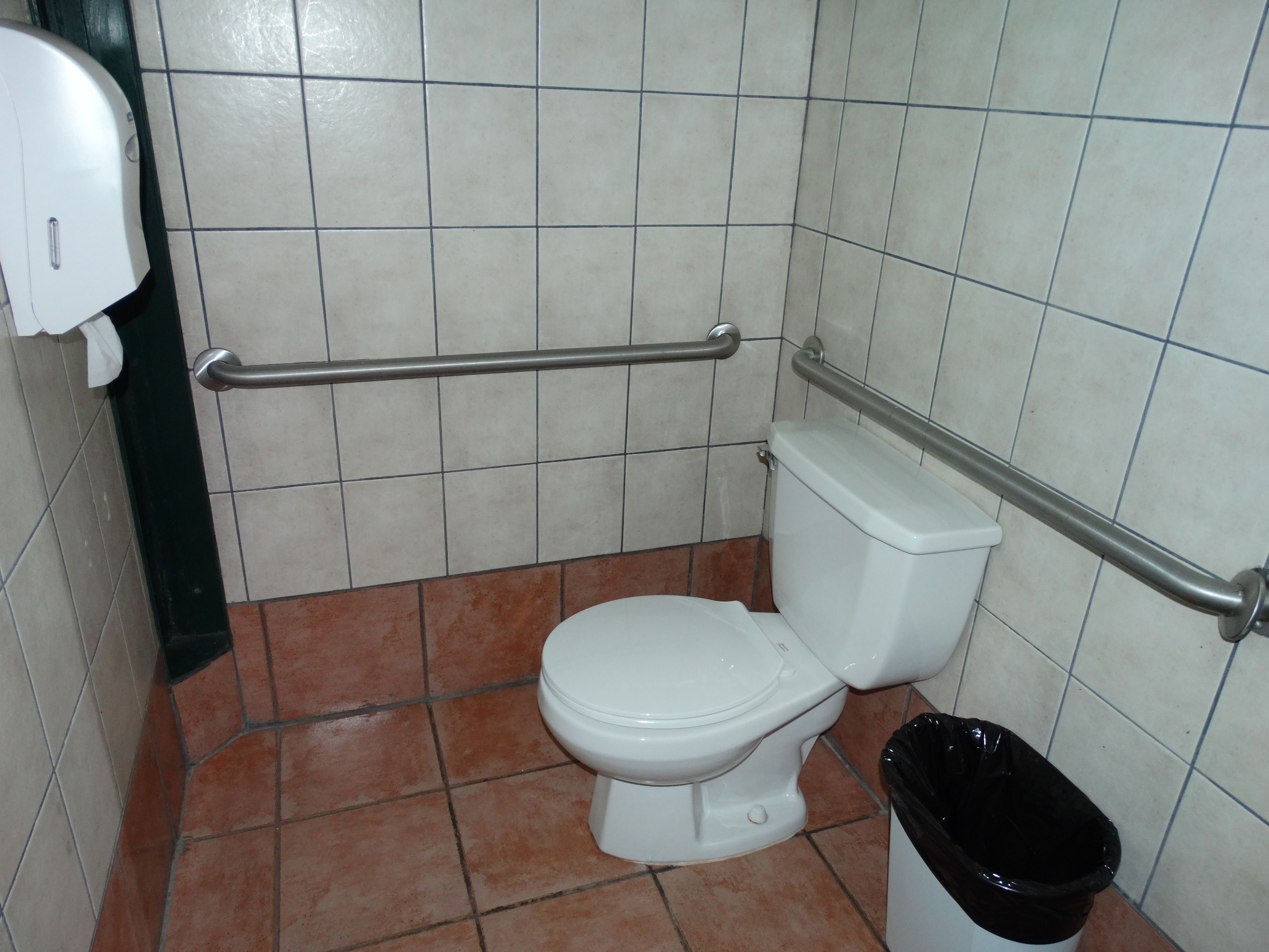 Une petite salle de bain avec des toilettes blanches, un sèche-mains et une poubelle.