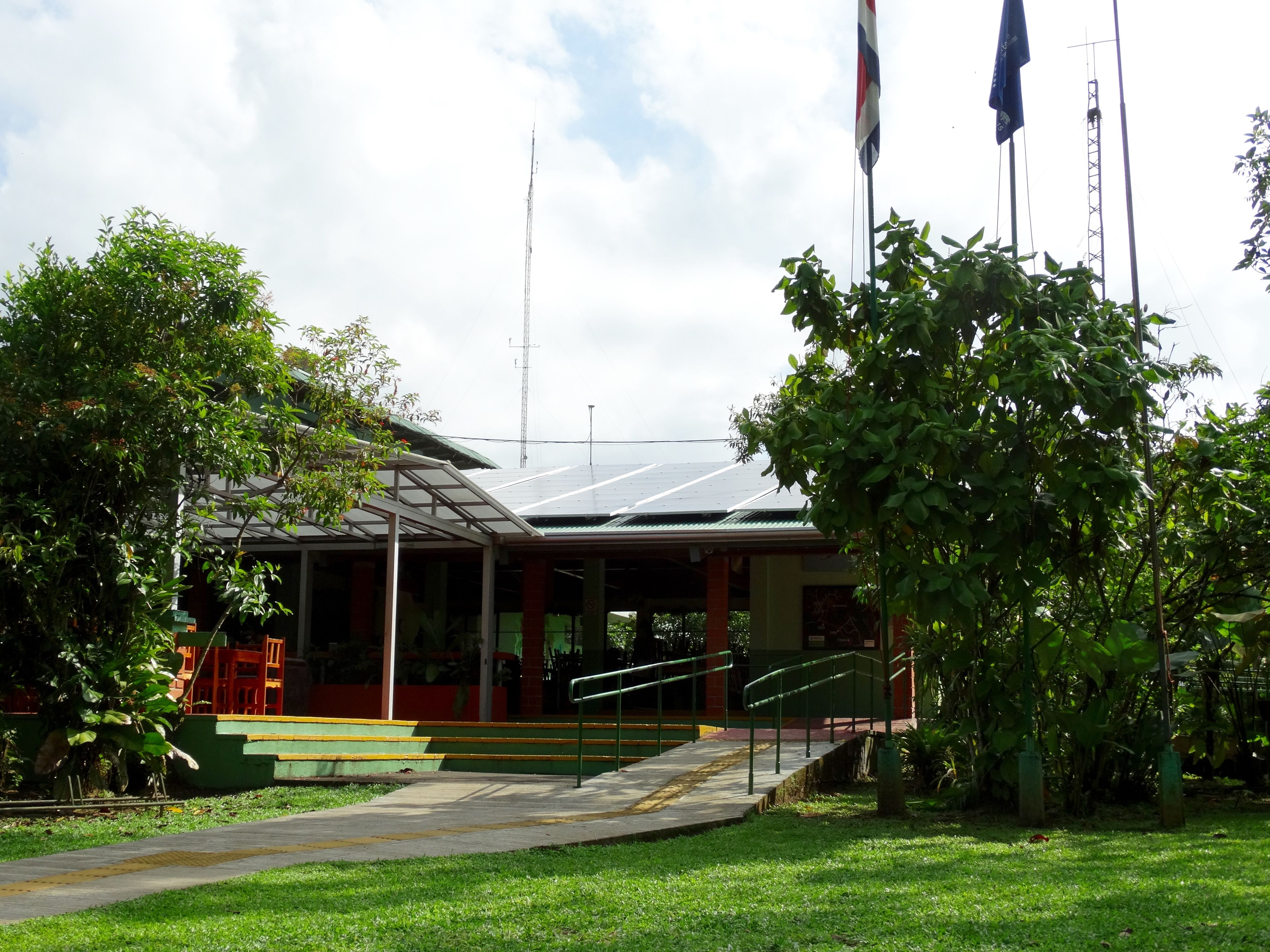 A building with a covered entrance, steps leading up to it, and a flagpole with flags.