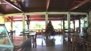A spacious indoor area with wooden tables and chairs, a counter with a stainless steel surface, and a green wall with a clock.