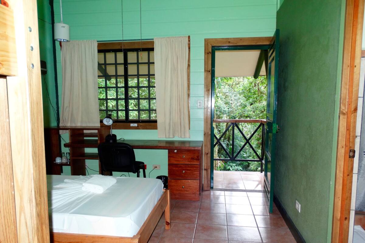 Una habitación con cama, escritorio, silla y ventana con cortinas.