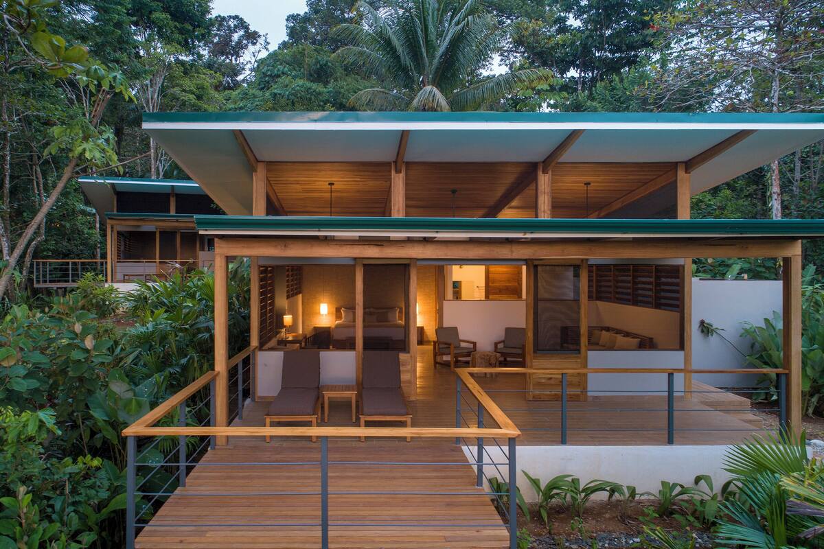 Ein modernes Haus mit einer Holzdachterrasse, Glasfassaden und einem begrünten Dach.