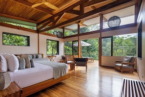 A spacious bedroom with a large bed, wooden ceiling beams, and large windows offering a view of the outdoors. - El Remanso Rainforest Lodge (Puerto Jiménez)