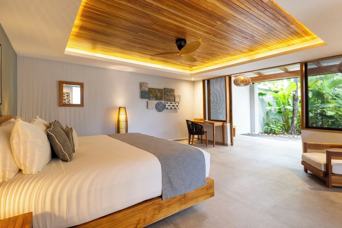 Ein modernes Schlafzimmer mit einem großen Bett, einem Schreibtisch und Blick auf Grün.