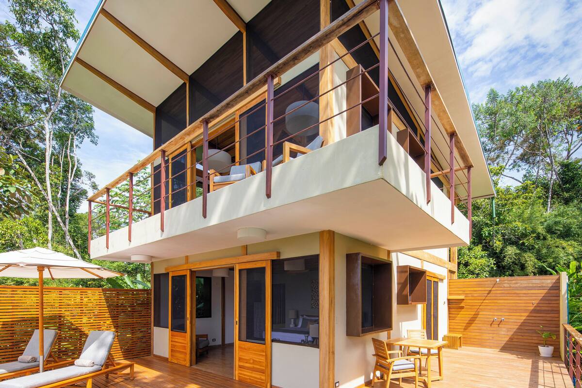 Ein zweistöckiges Haus mit einer Holzterrasse, einem Swimmingpool und Gartenmöbeln.