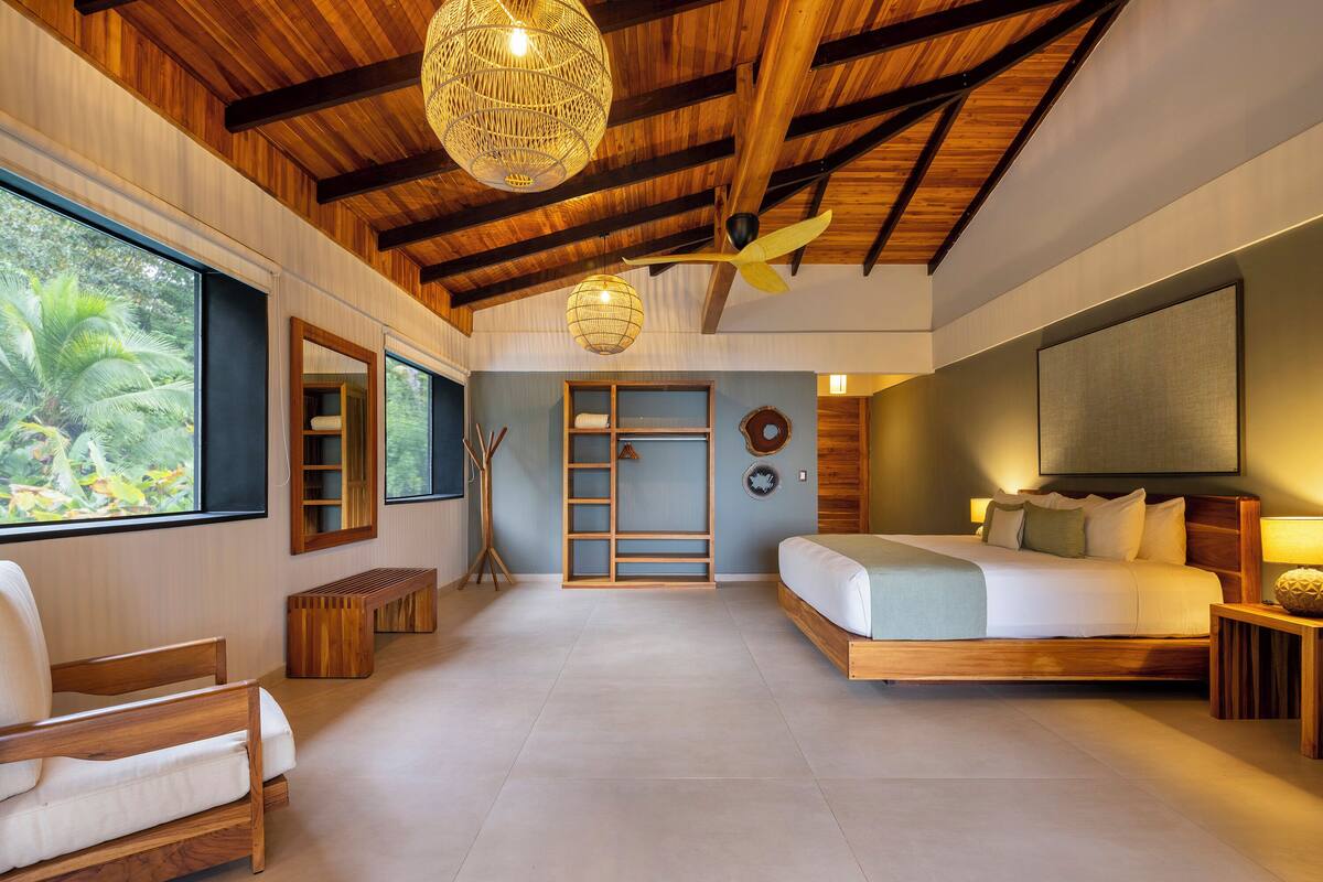 Ein geräumiges Schlafzimmer mit einem großen Bett, einer Holzzieldecke und Blick auf Grün.