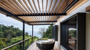 A balcony with a wooden deck, a black chair, and a view of a lush landscape. - El Remanso Rainforest Lodge (Puerto Jiménez)