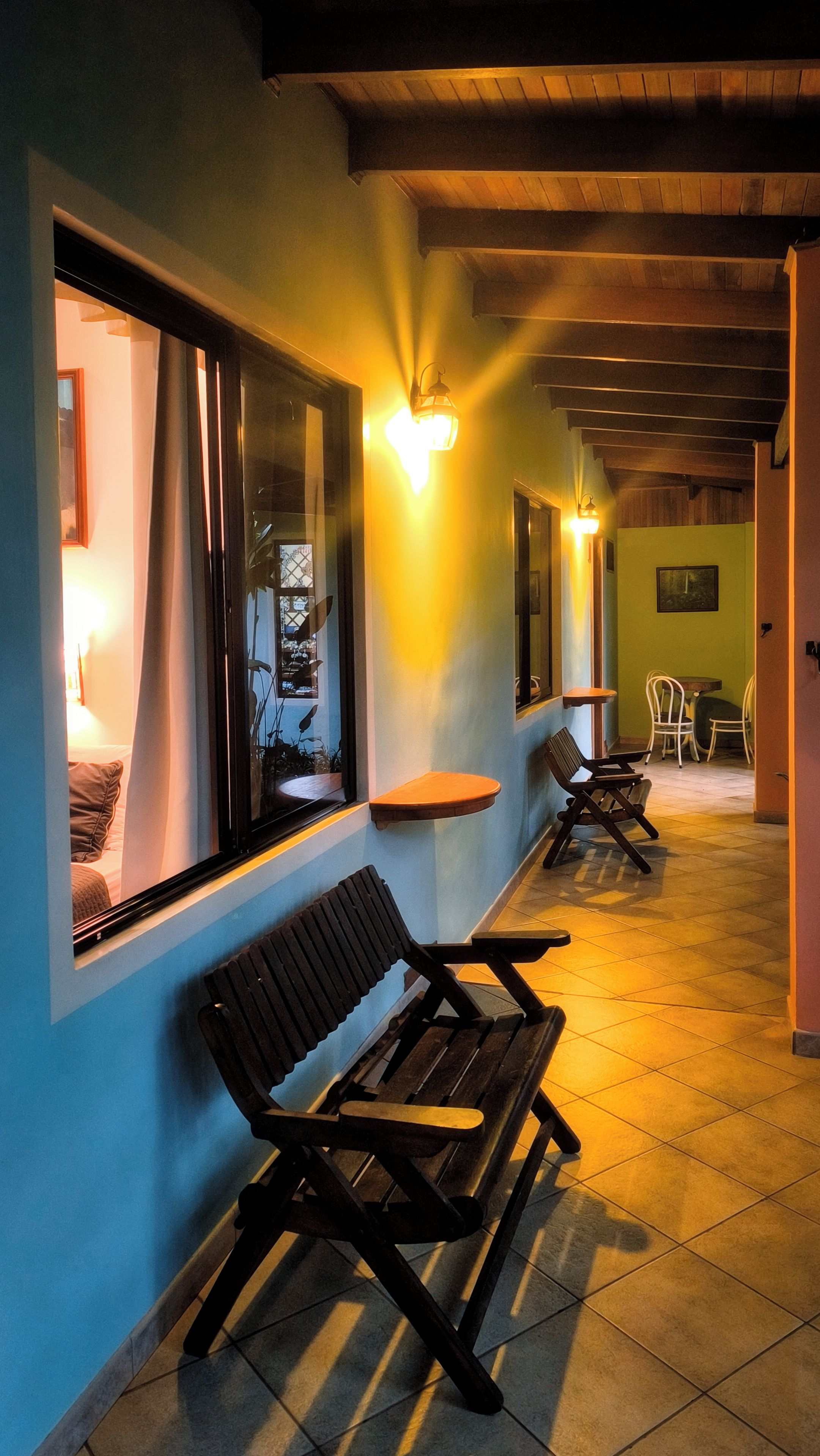 A corridor with benches, a table, and chairs, leading to a dining area with a view of the outside.
