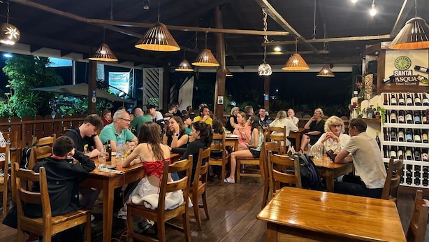 A restaurant with wooden tables and chairs, hanging pendant lights, and a wine rack in the background. - Hotel Arte Natura (La Fortuna)