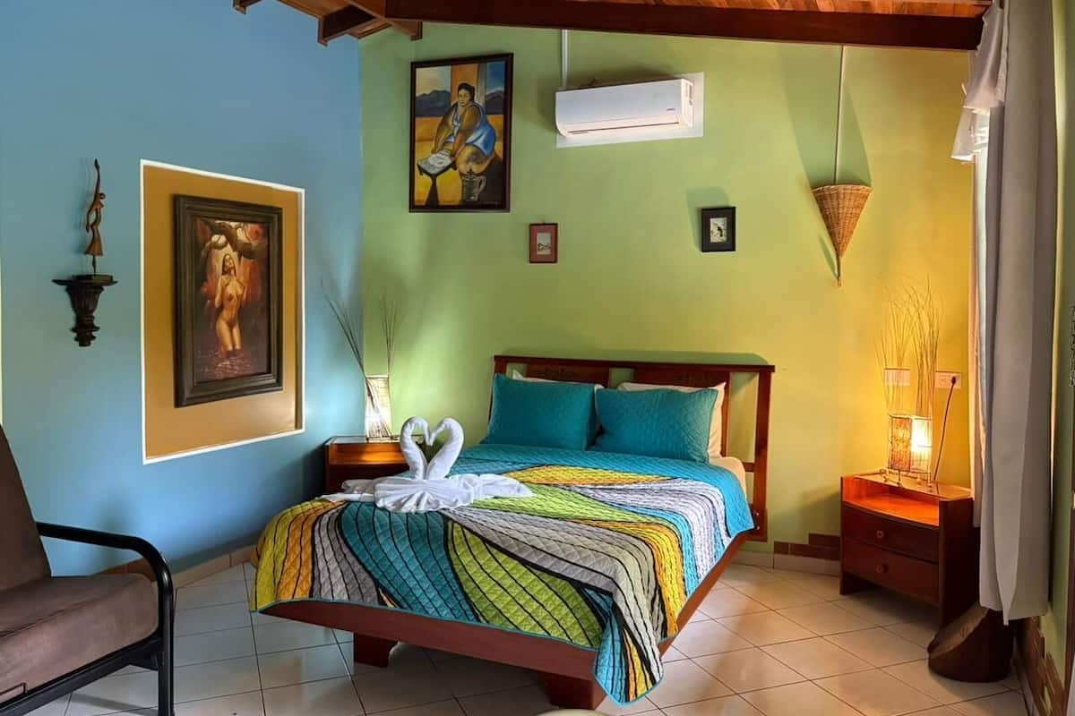Une chambre à coucher comprenant un lit, une chaise, une table de chevet et un climatiseur fixé au mur.