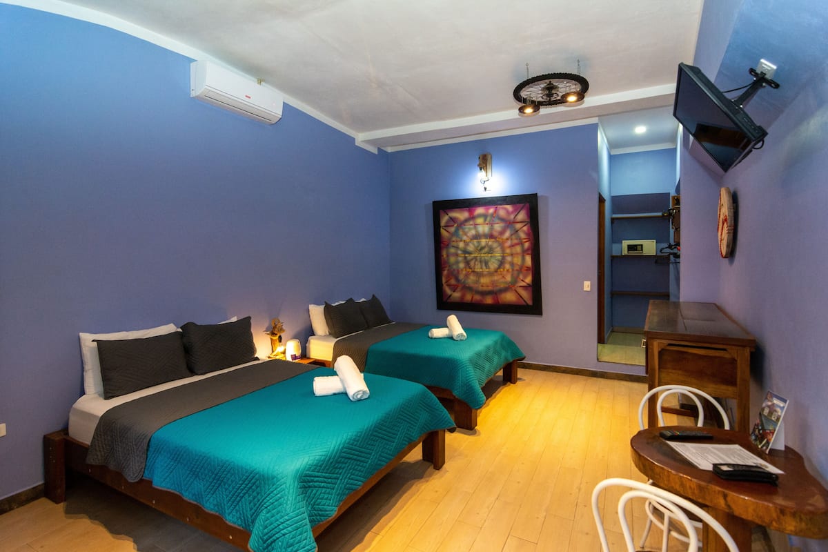 Une chambre d’hôtel avec deux lits, un téléviseur fixé au mur et une table en bois avec des chaises.