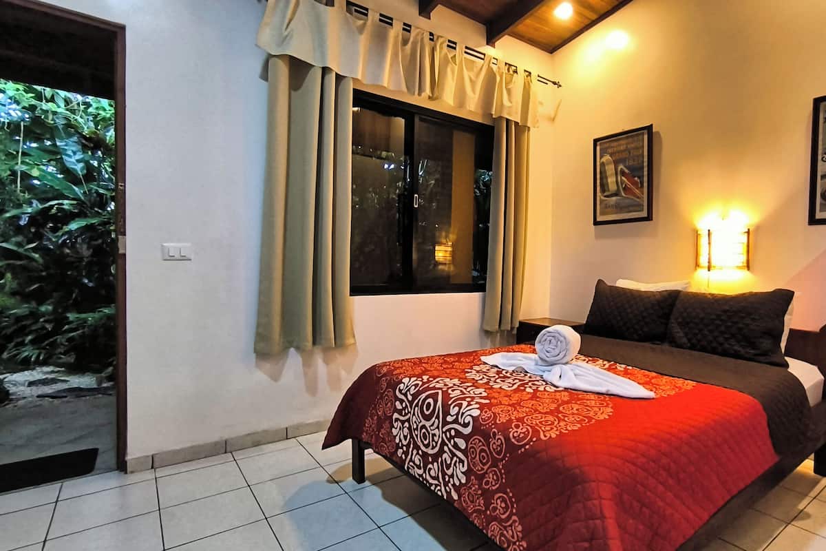 Une chambre d’hôtel avec un lit, une fenêtre avec des rideaux, une lampe fixée au mur et une affiche.