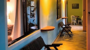 A corridor with benches, a table, and chairs, leading to a dining area with a view of the outside. - Hotel Arte Natura (La Fortuna)