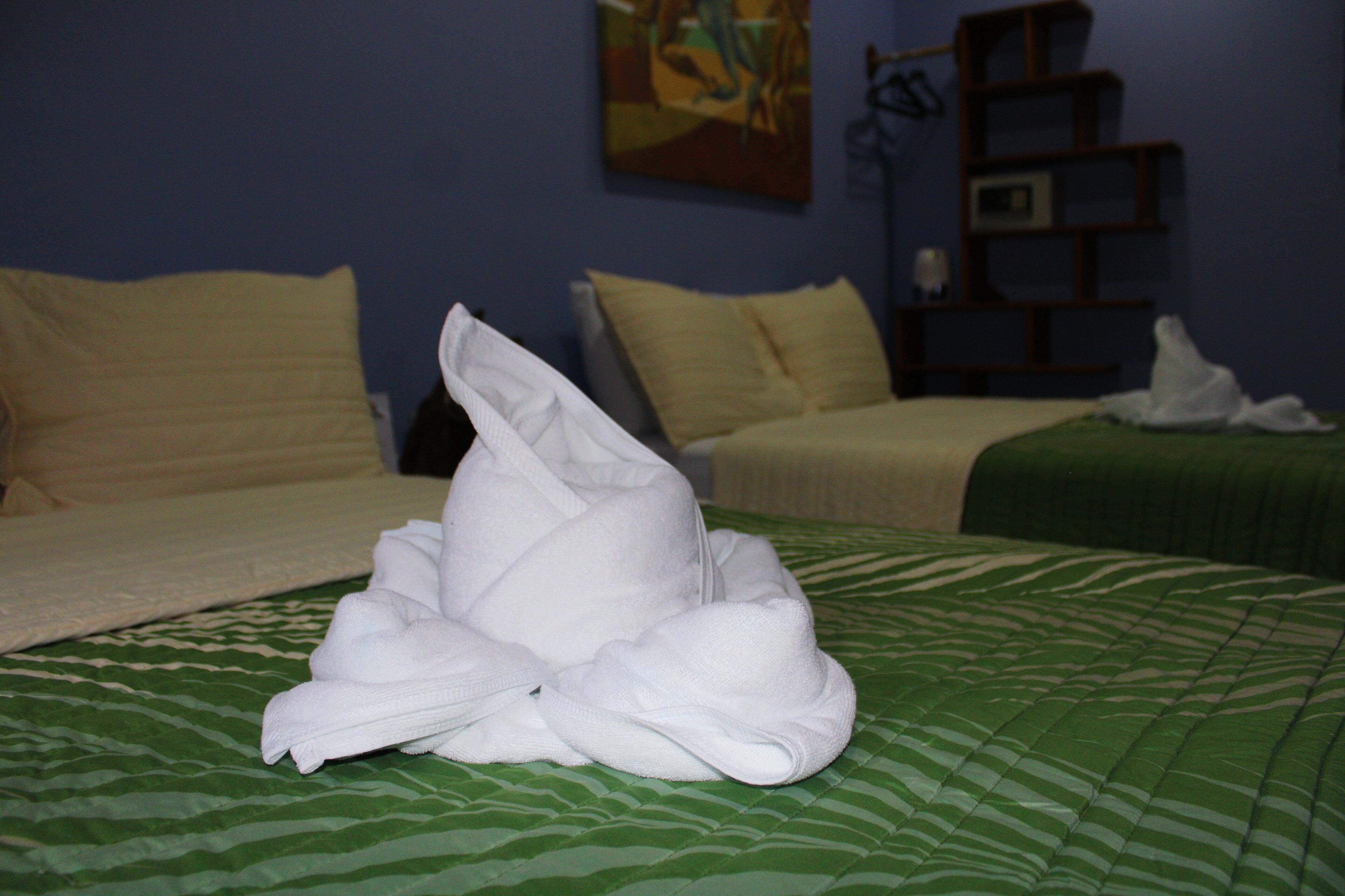 Una cama bien tendida con una colcha verde estampada y toallas blancas dobladas en el centro.