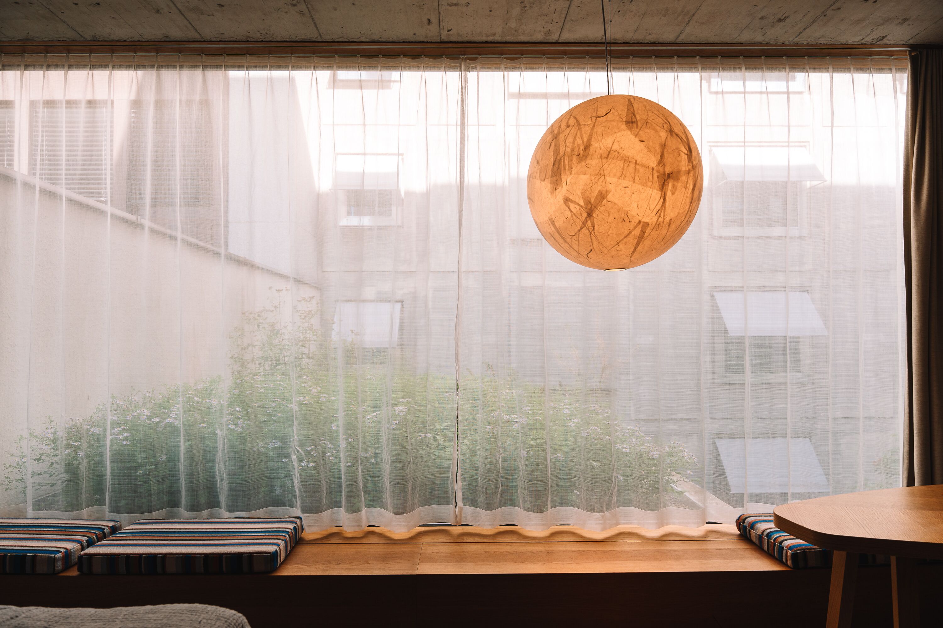 A room with a large window, a round wooden light fixture, and a bench with striped cushions.