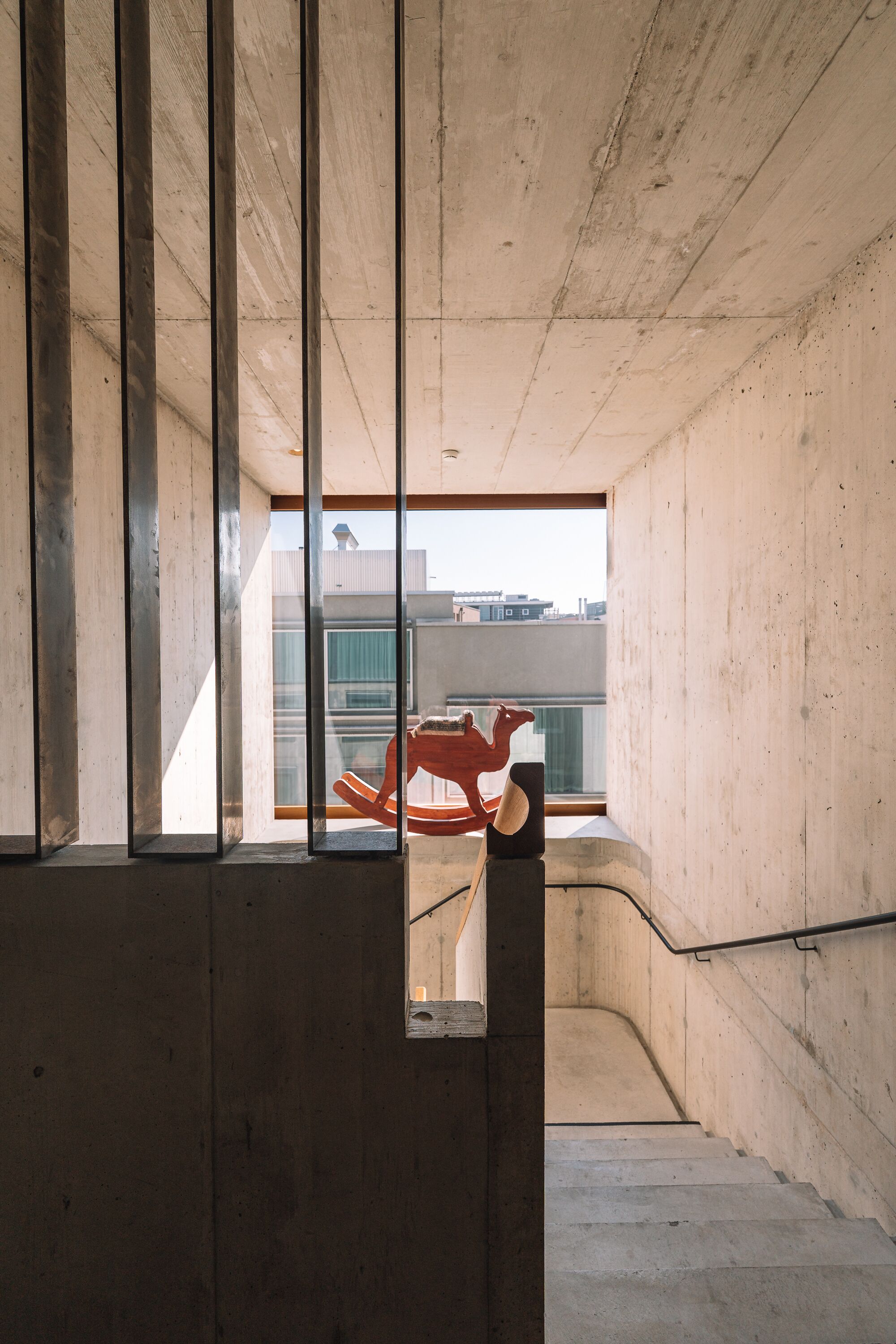 Interior de hormigón con ventana, una escalera y vistas a edificios.