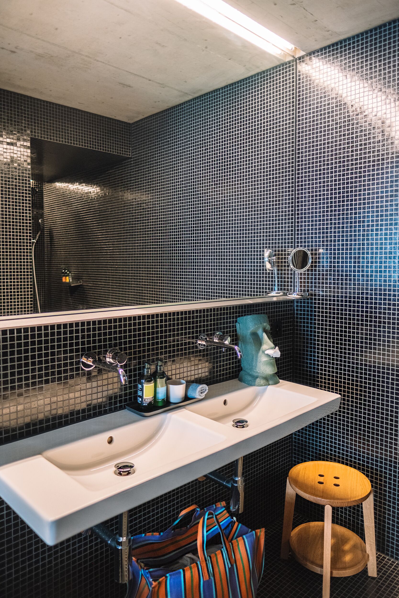 A bathroom with a white sink, a mirror, a towel dispenser, and a striped bag on the floor.