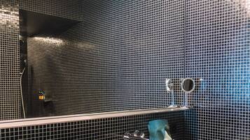 A bathroom with a white sink, a mirror, a towel dispenser, and a striped bag on the floor.