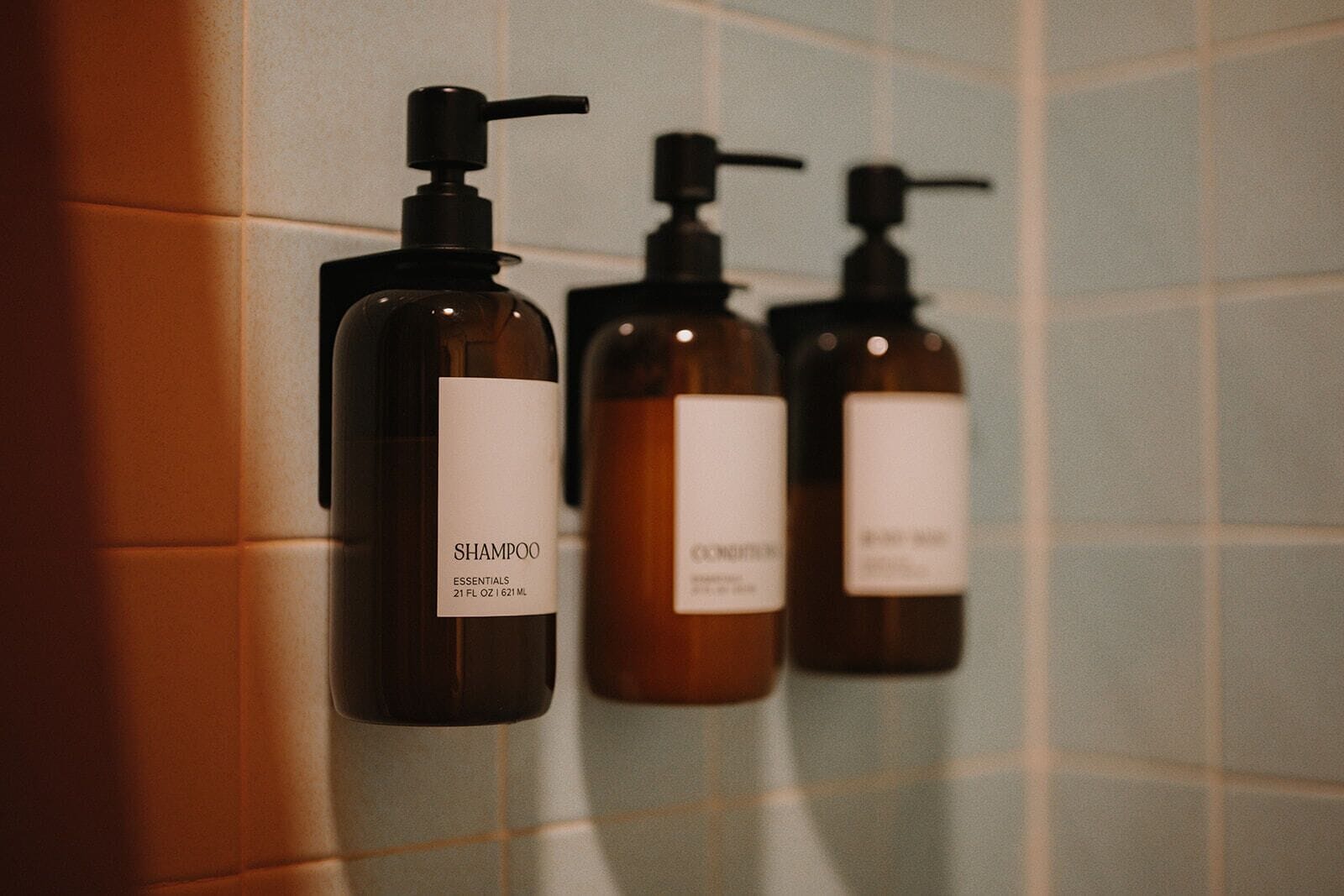 Three shampoo bottles with pump dispensers mounted on a tiled wall.