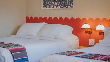 A hotel room with two beds, a bench, a painting on the wall, and two wall lamps.