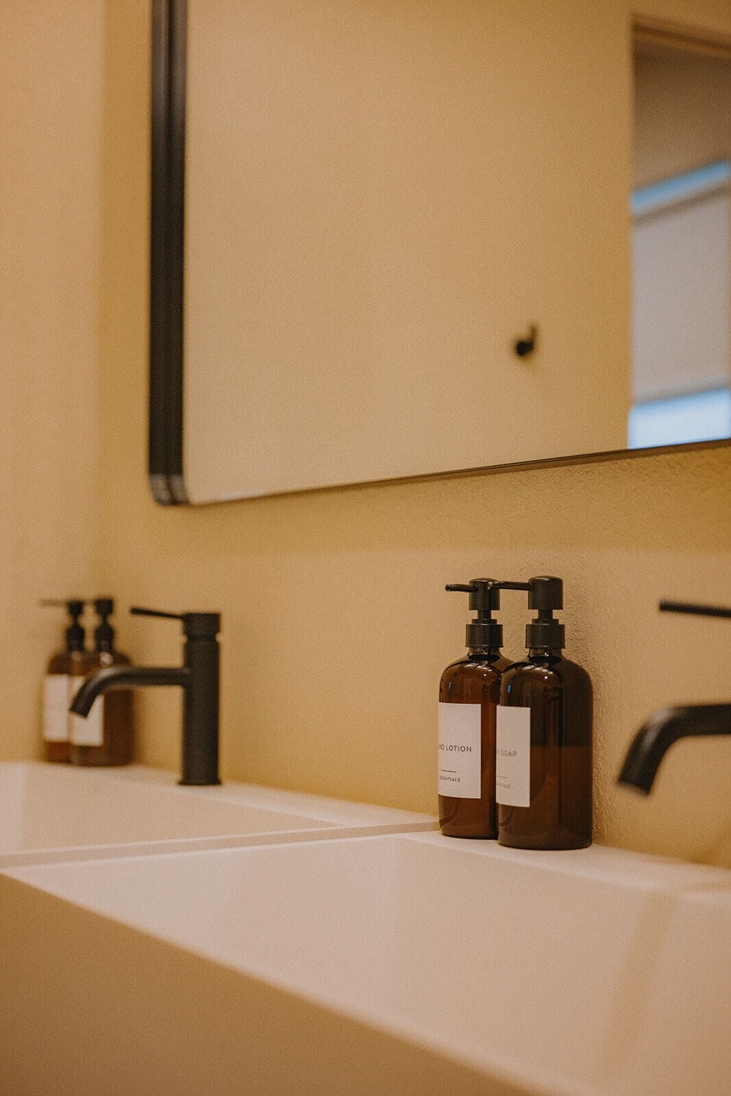 A bathroom with a white sink, two brown soap dispensers, a black faucet, and a mirror above the sink.