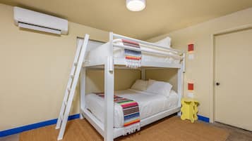 A bunk bed with a ladder, white bedding, a colorful blanket, a small yellow stool, and an air conditioning unit on the wall.