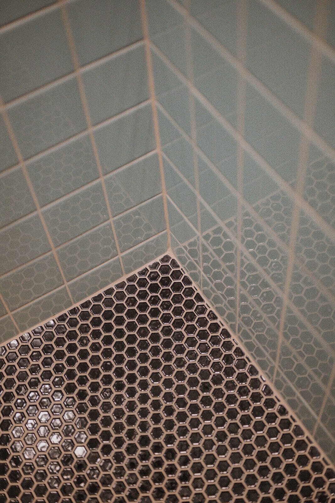 A corner of a bathroom with a hexagonal tile pattern on the floor and square tiles on the walls.