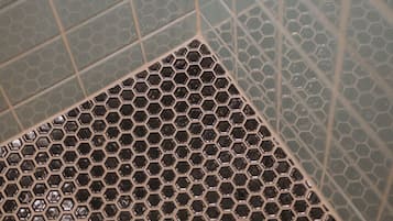 A corner of a bathroom with a hexagonal tile pattern on the floor and square tiles on the walls.