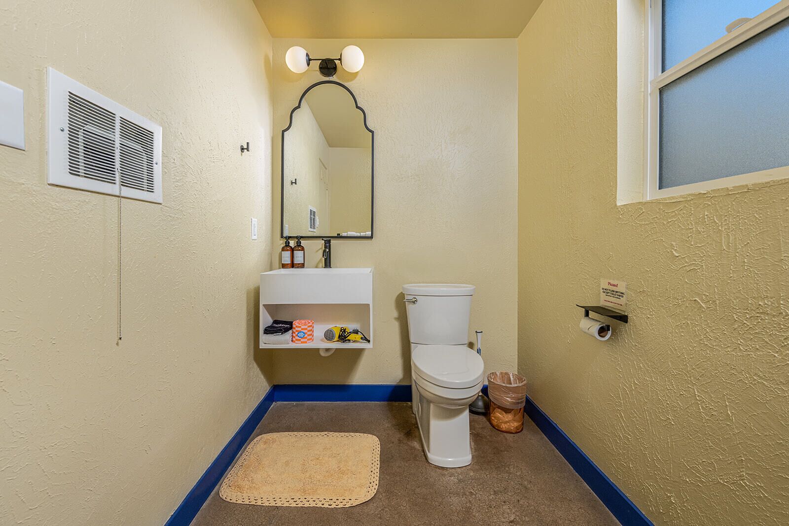 A bathroom with a toilet, sink, mirror, and a blue mat on the floor.