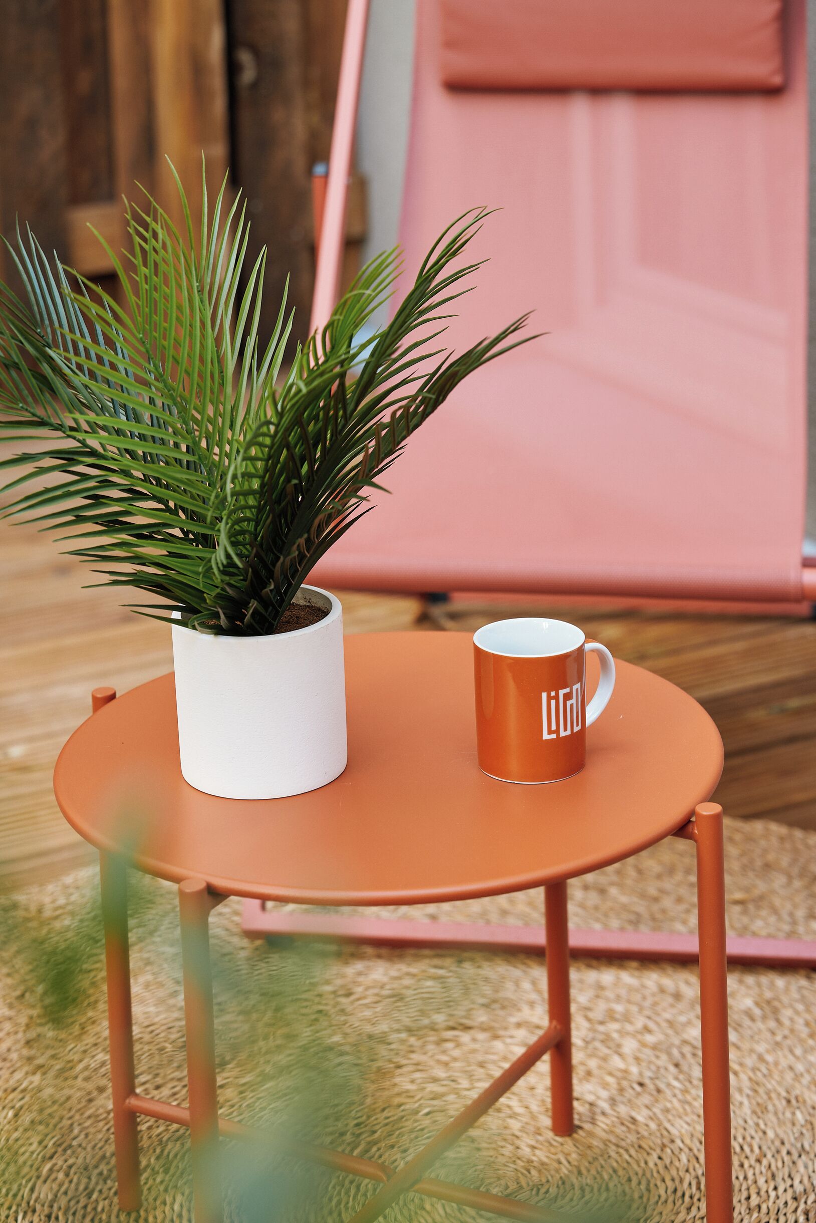 A small round table with a white pot and an orange mug.