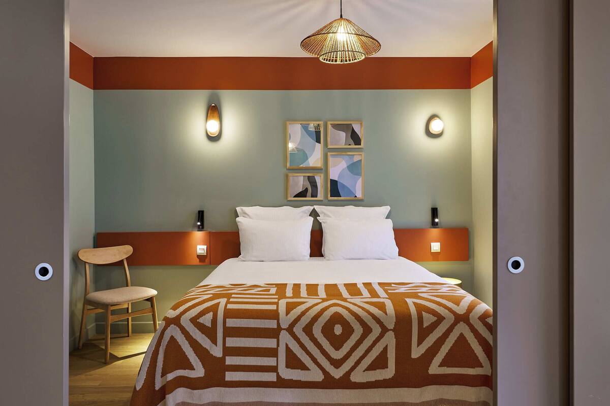 Une chambre d’hôtel avec un lit, une chaise et un luminaire fixé au mur.