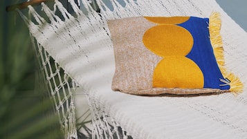 A hammock with macrame netting, a cushion with a geometric pattern, and a wooden support.