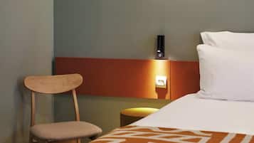 A hotel room with a bed, a chair, a nightstand, and a wall-mounted light fixture.